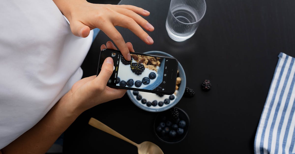 Person photographing a berry and yogurt bowl with a smartphone at breakfast.