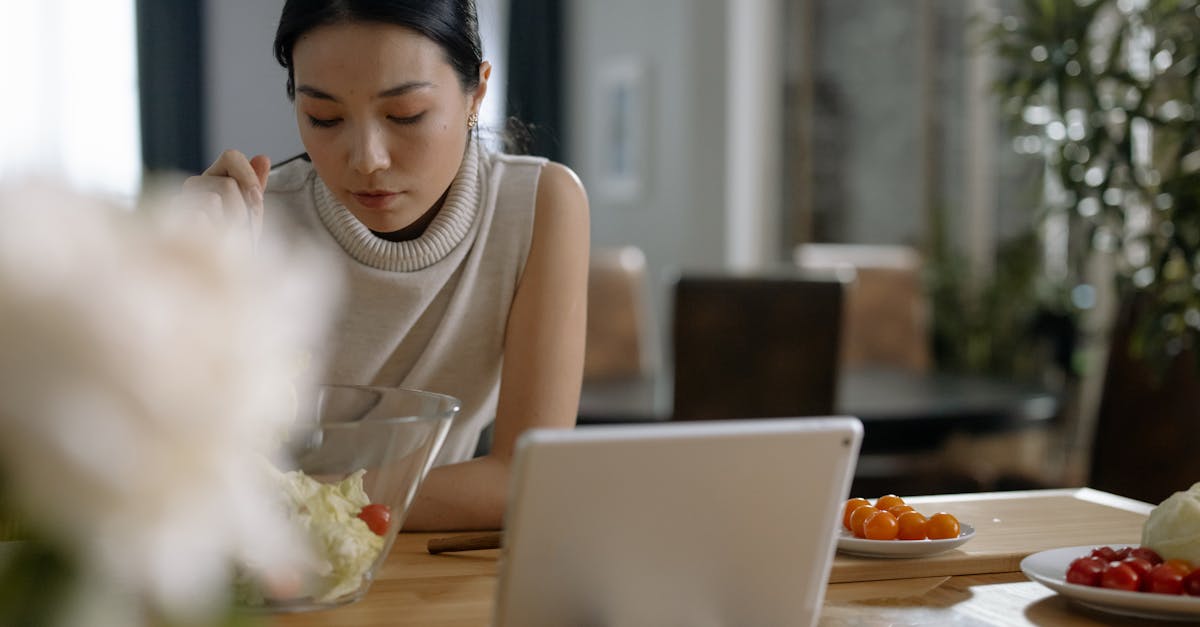 Asian woman using tablet while preparing salad in modern kitchen.