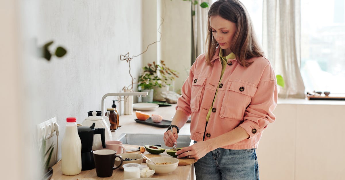 A woman slices an avocado in a bright, modern kitchen with natural light.