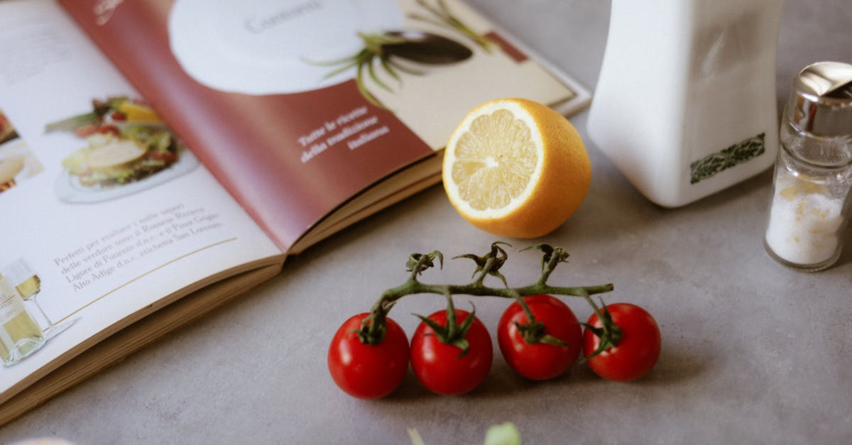 Flat lay of cooking ingredients including tomatoes and a lemon with a cookbook.