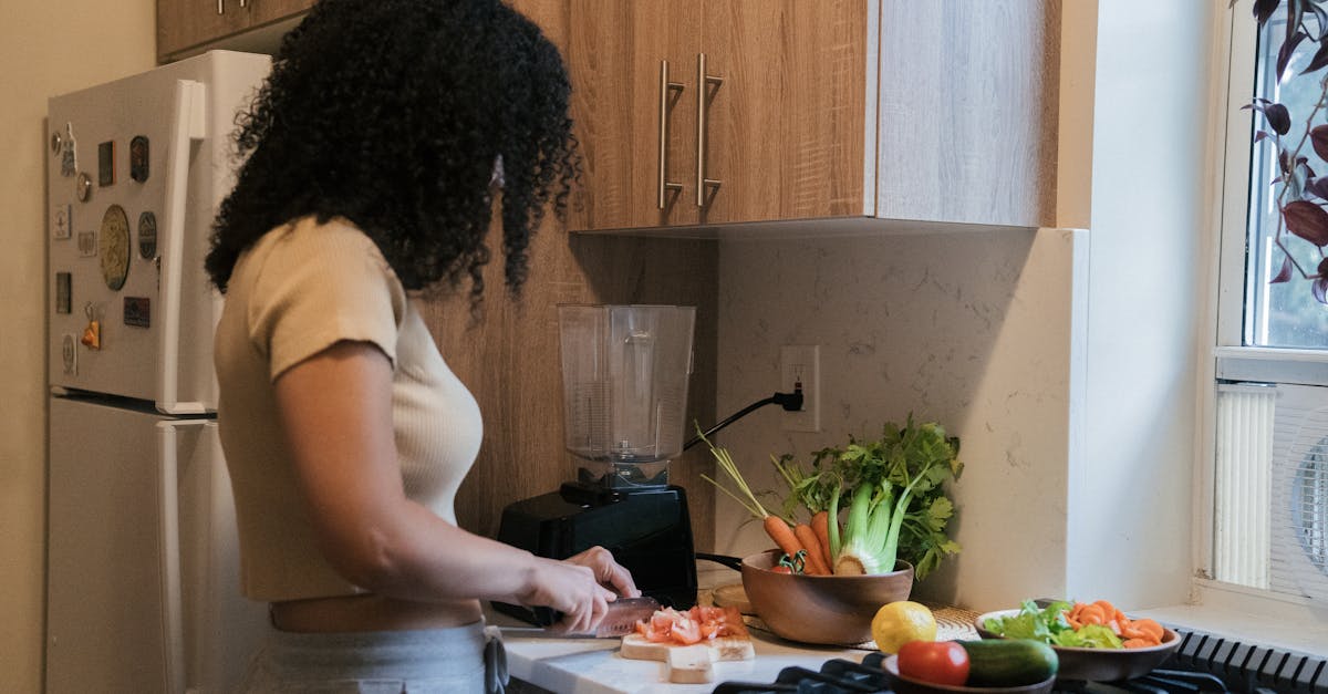 A woman cuts vegetables on a board in a modern kitchen setting, surrounded by fresh produce.