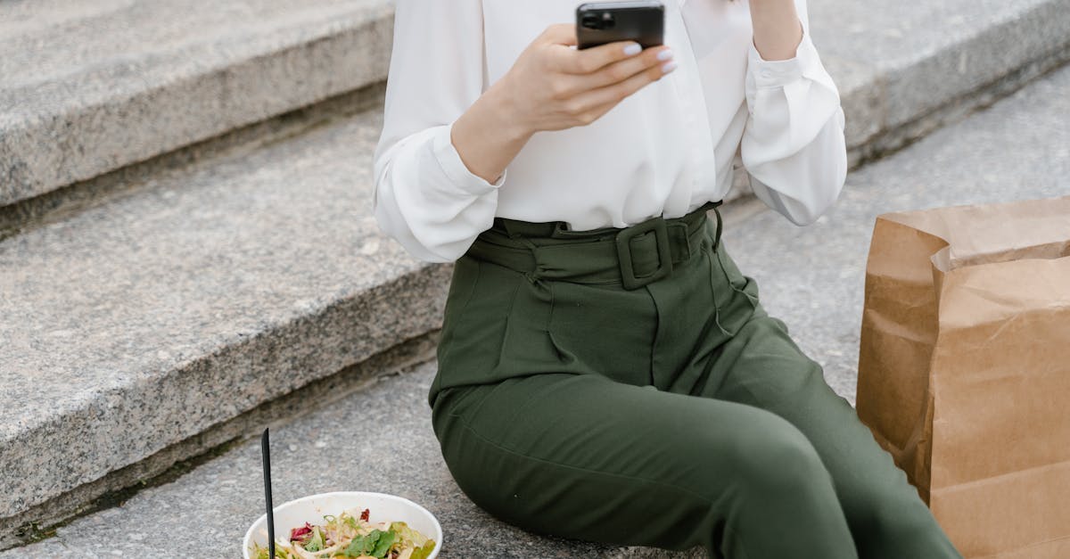 A woman sits on concrete steps with a salad and paper bag, using a smartphone.