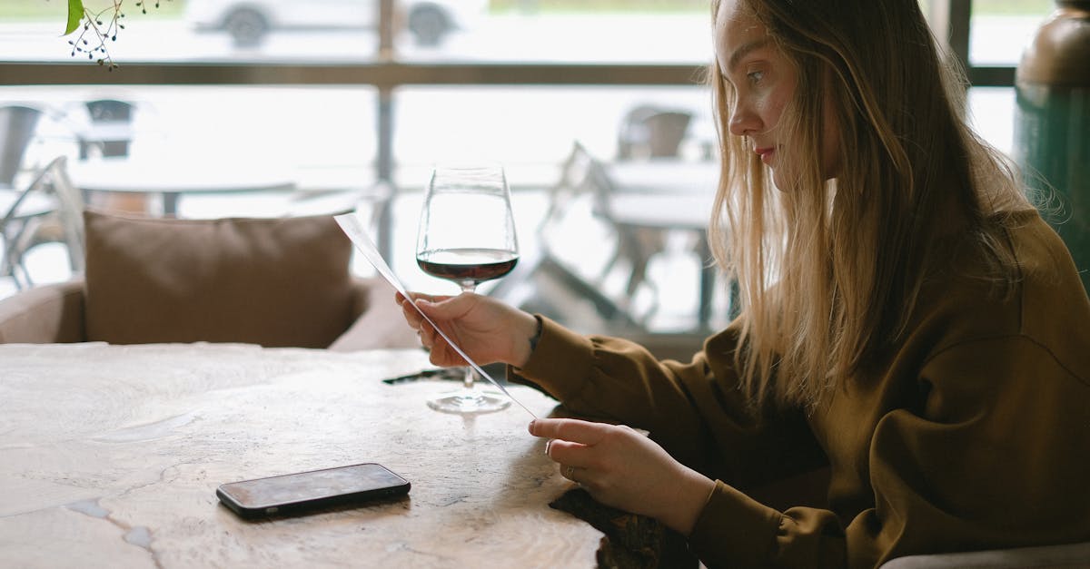 A woman with long hair is reading a menu while sipping wine in a cozy restaurant.