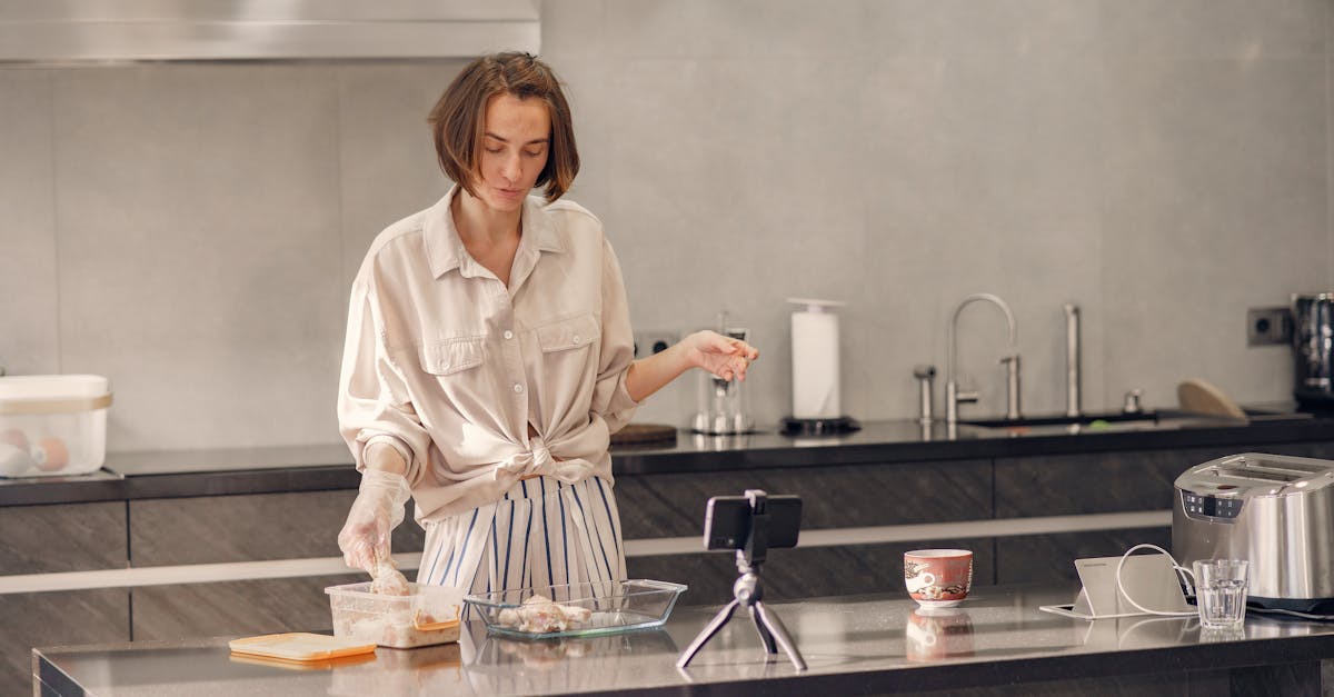 A woman preparing chicken in a contemporary kitchen, using a smartphone for guidance.