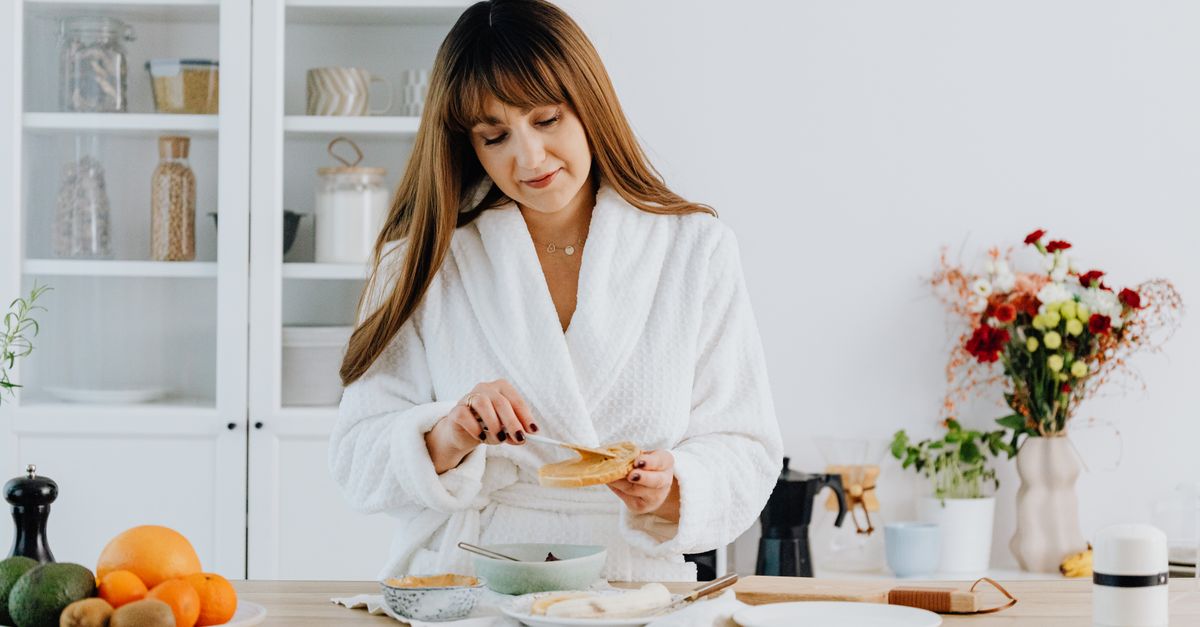 A woman in a bathrobe preparing breakfast in a home kitchen.