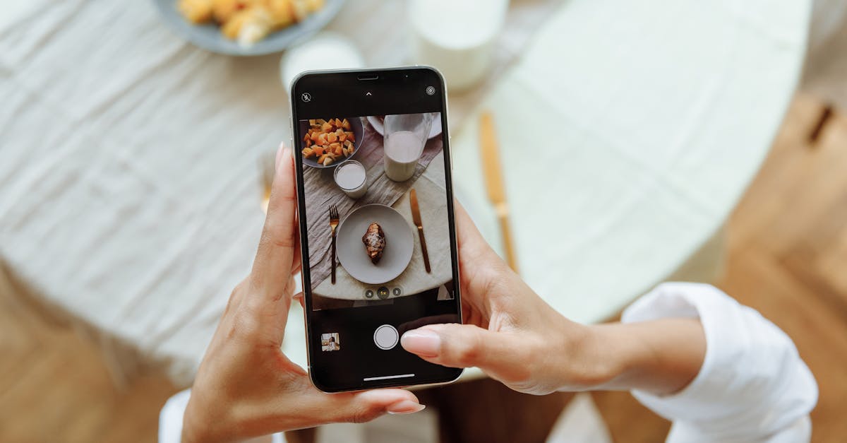 A person taking a photo of a breakfast setup with a smartphone on a table indoors.